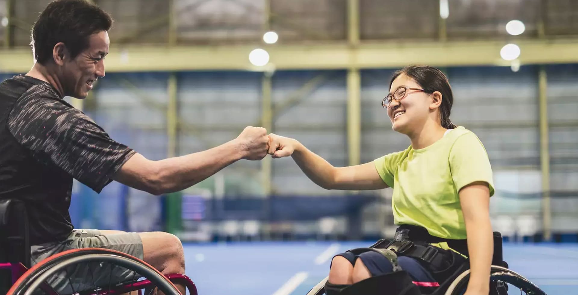 Man and young woman in wheelchairs giving a fist bump